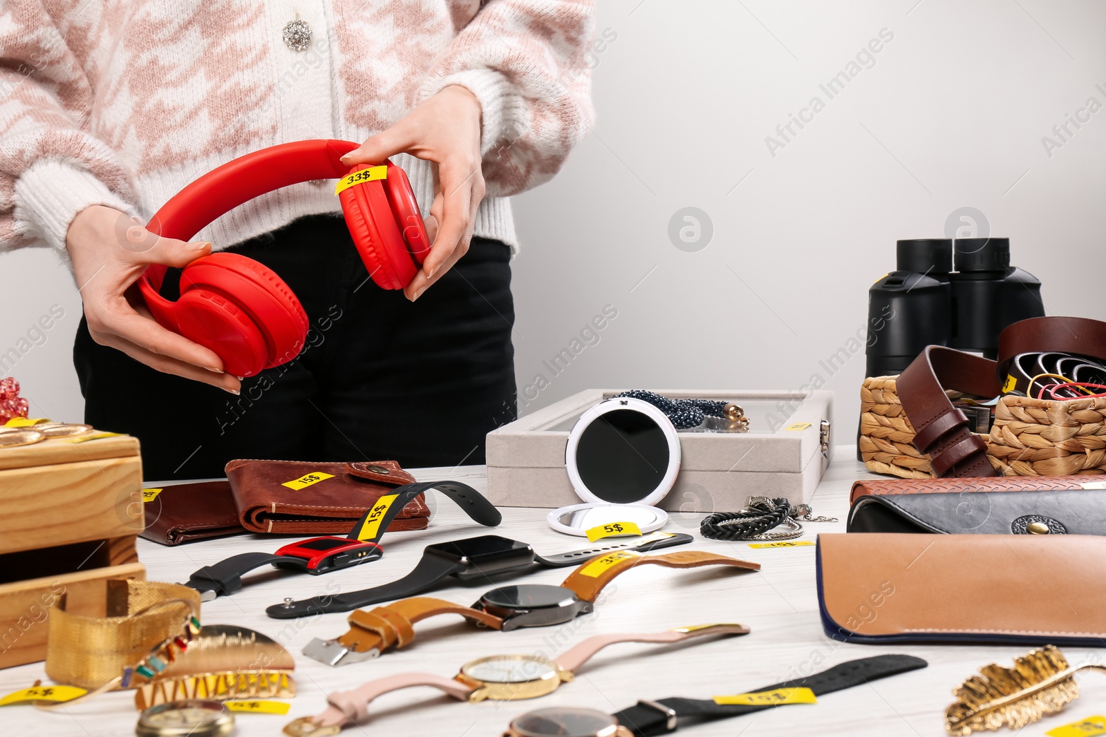 Photo of Woman holding headphones near table with different stuff indoors, closeup. Garage sale