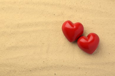 Photo of Honeymoon concept. Two red wooden hearts on sand, space for text