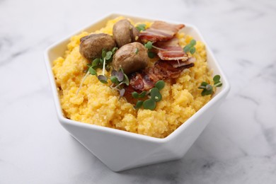 Photo of Cooked cornmeal with bacon, mushrooms and microgreens in bowl on white marble table, closeup