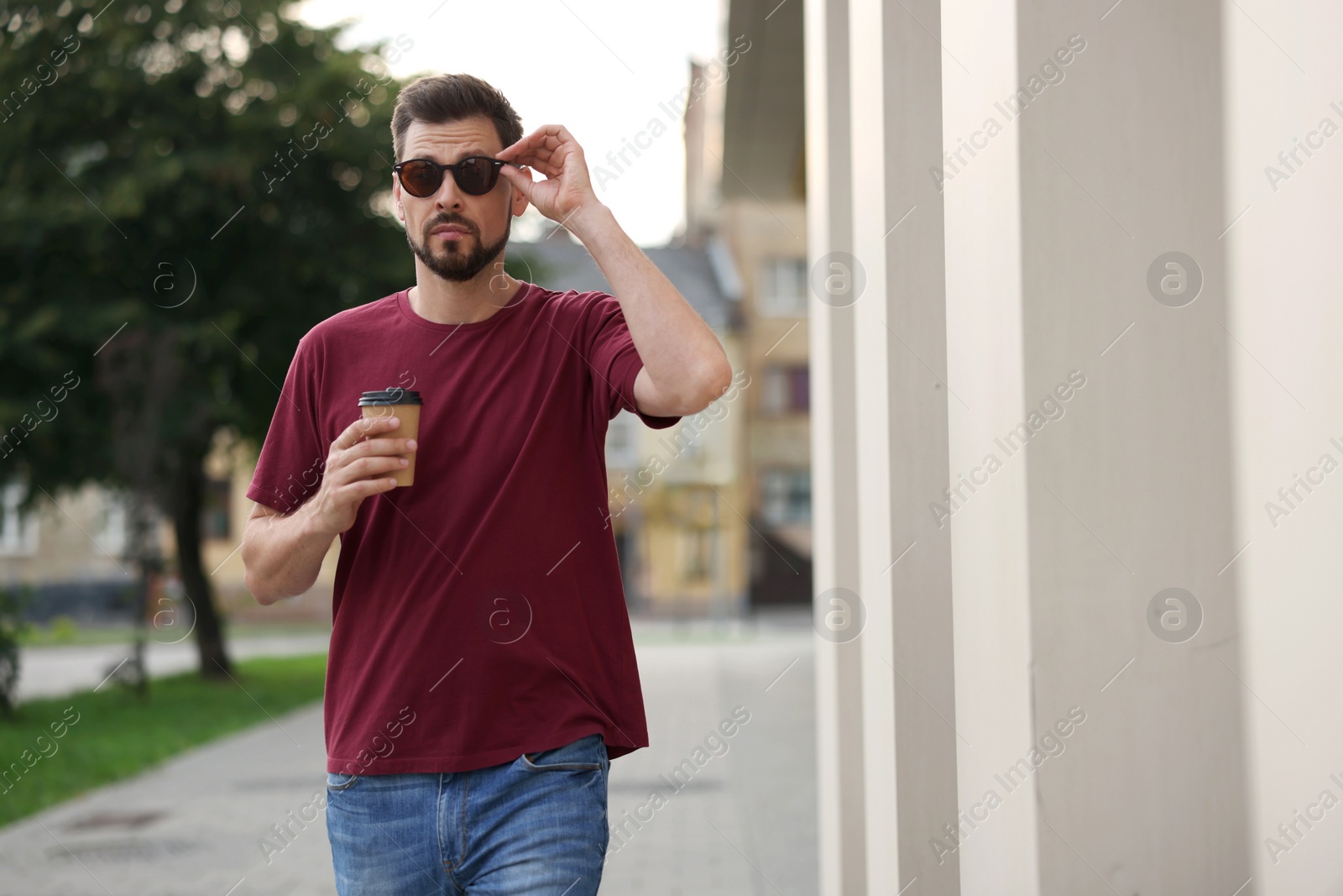 Photo of Handsome man with cup of drink walking on city street