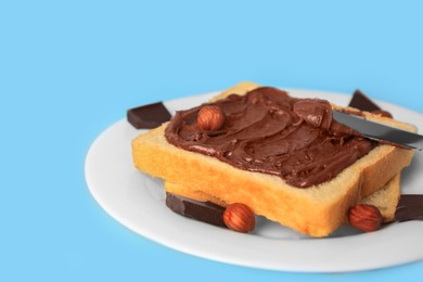 Photo of Spreading chocolate paste onto bread on light blue background, closeup. Space for text