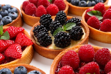 Photo of Tartlets with different fresh berries on white table, closeup. Delicious dessert