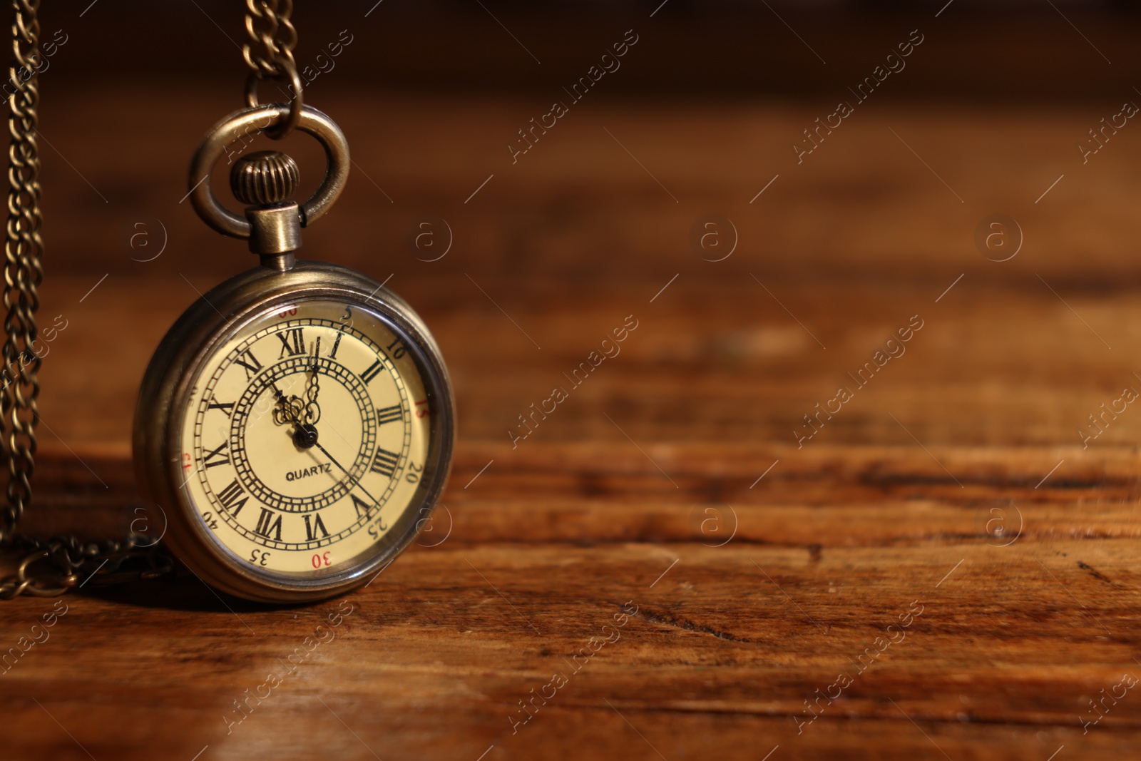 Photo of Pocket clock with chain on wooden table, closeup. Space for text