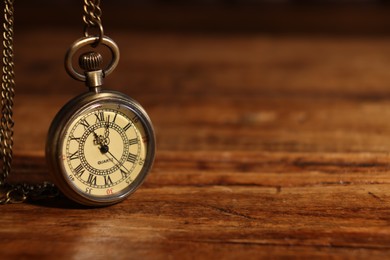 Photo of Pocket clock with chain on wooden table, closeup. Space for text