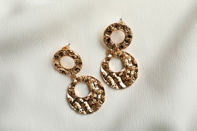 Photo of Elegant golden earrings on white fabric, flat lay. Stylish bijouterie