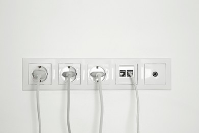 Photo of Many power sockets with plugs, ethernet and TV coax plates on white wall indoors