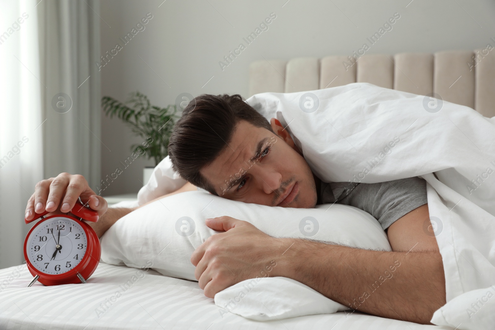 Photo of Emotional man with alarm clock in bed. Being late because of oversleeping