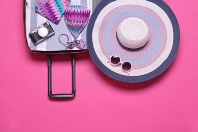 Photo of Open suitcase with beach objects on pink background, top view