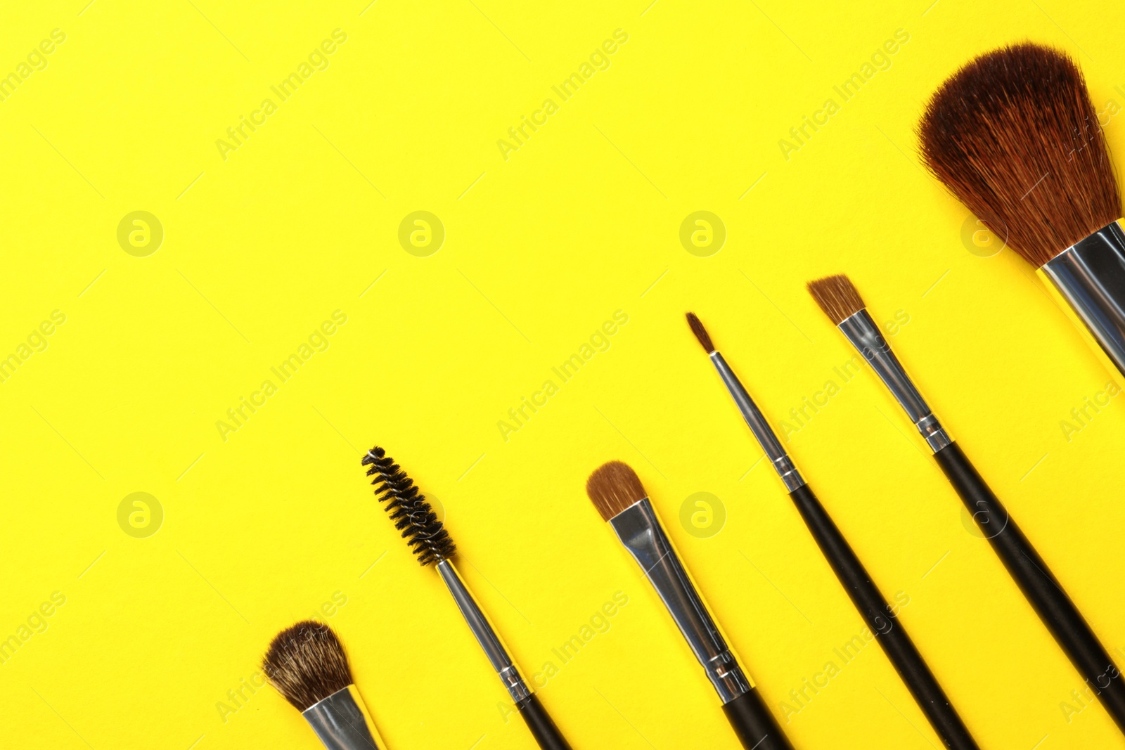 Photo of Set of makeup brushes on yellow background, flat lay. Space for text