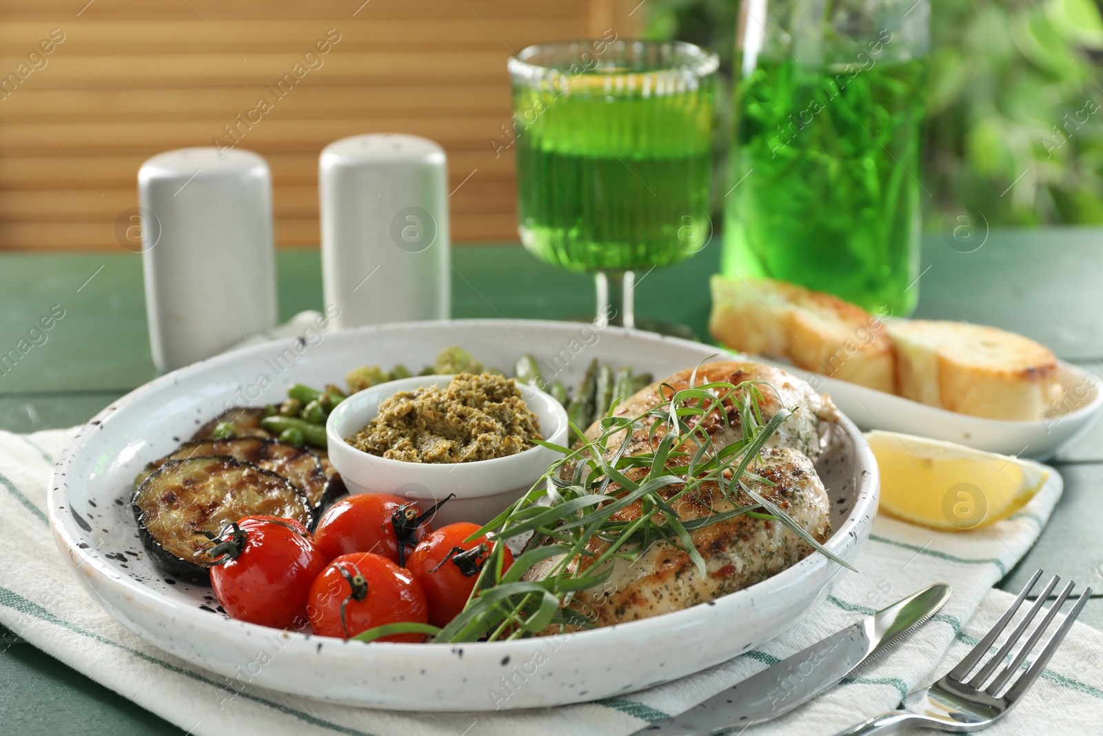 Photo of Tasty chicken, vegetables with tarragon and pesto sauce served on green table, closeup
