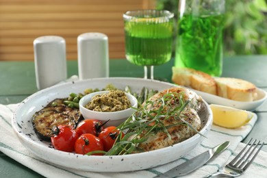 Photo of Tasty chicken, vegetables with tarragon and pesto sauce served on green table, closeup