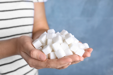 Woman holding heap of refined sugar cubes on blue background, closeup