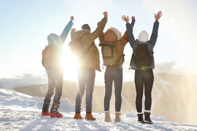 Photo of Group of excited friends with backpacks enjoying mountain view during winter vacation