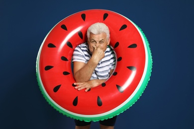 Photo of Funny mature man with bright inflatable ring on dark blue background