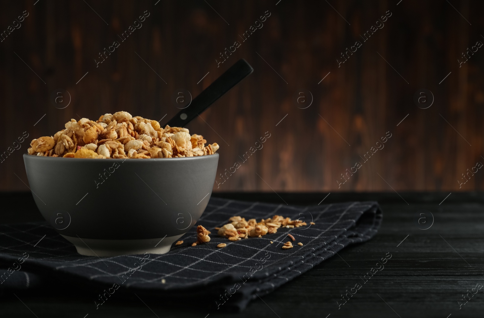 Photo of Ceramic bowl with granola on black wooden table, space for text. Cooking utensil