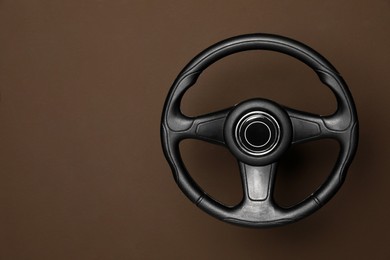 Photo of New black steering wheel on brown background, space for text