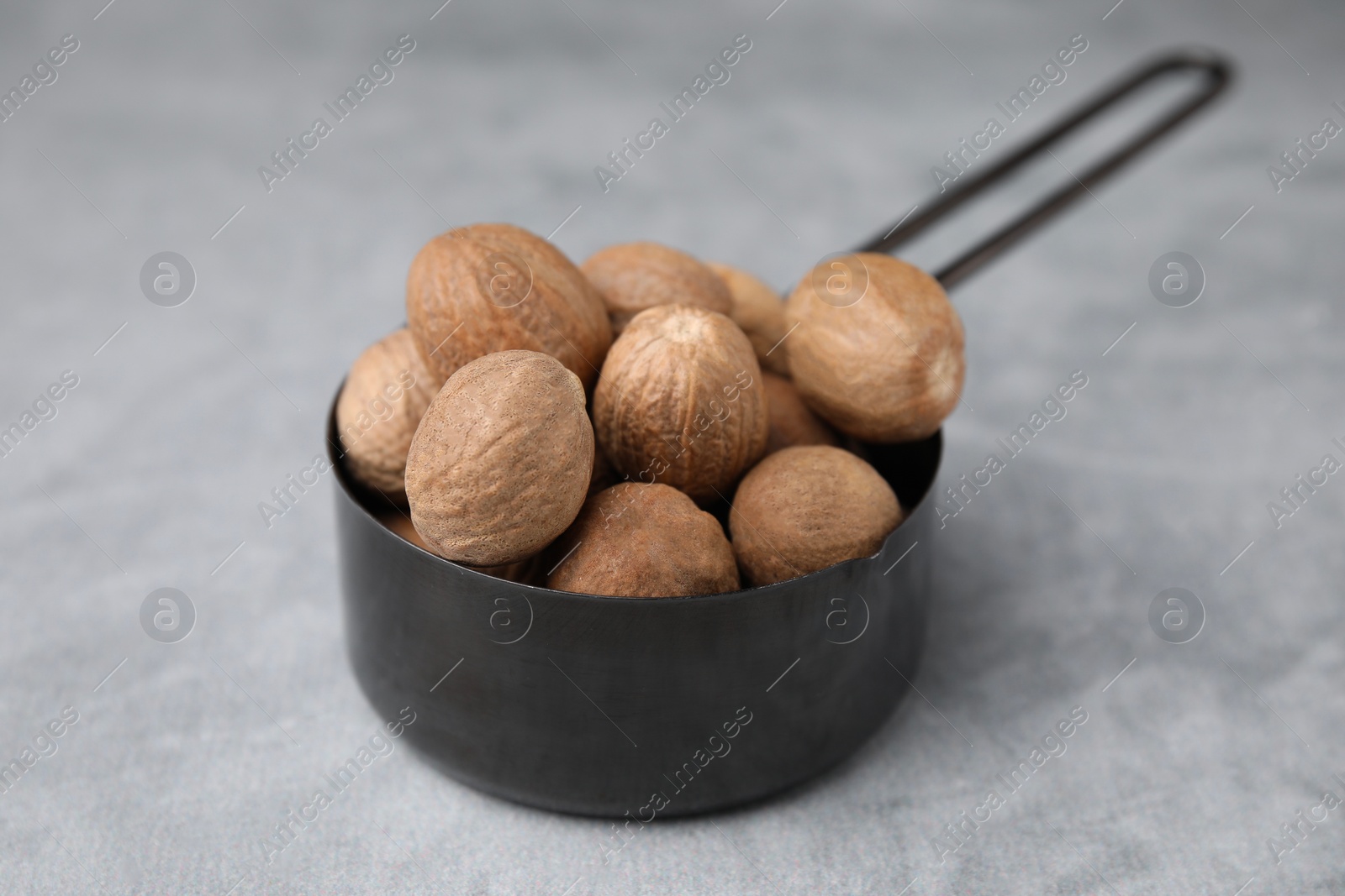 Photo of Whole nutmegs in small saucepan on light grey table, closeup