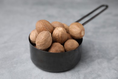 Photo of Whole nutmegs in small saucepan on light grey table, closeup