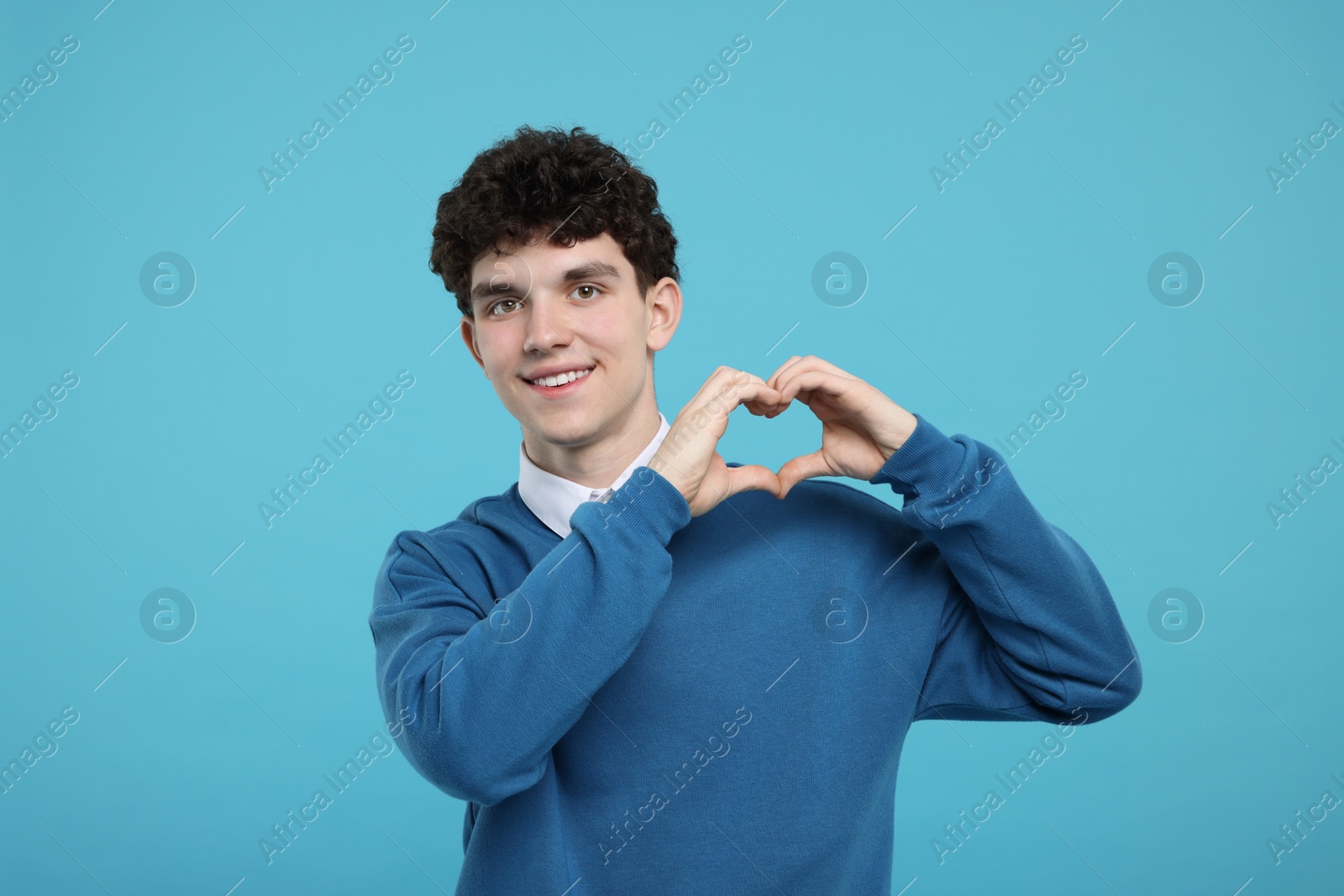 Photo of Happy young man showing heart gesture with hands on light blue background