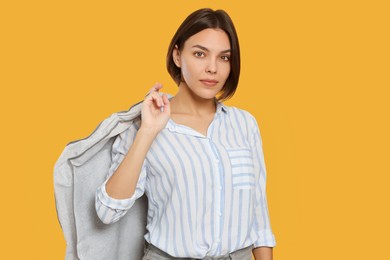Photo of Woman holding garment cover with clothes on yellow background. Dry-cleaning service