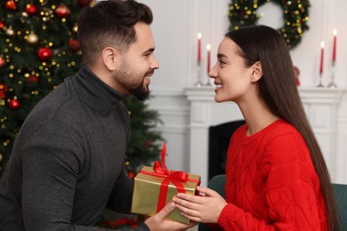 Happy man giving Christmas gift to his girlfriend at home
