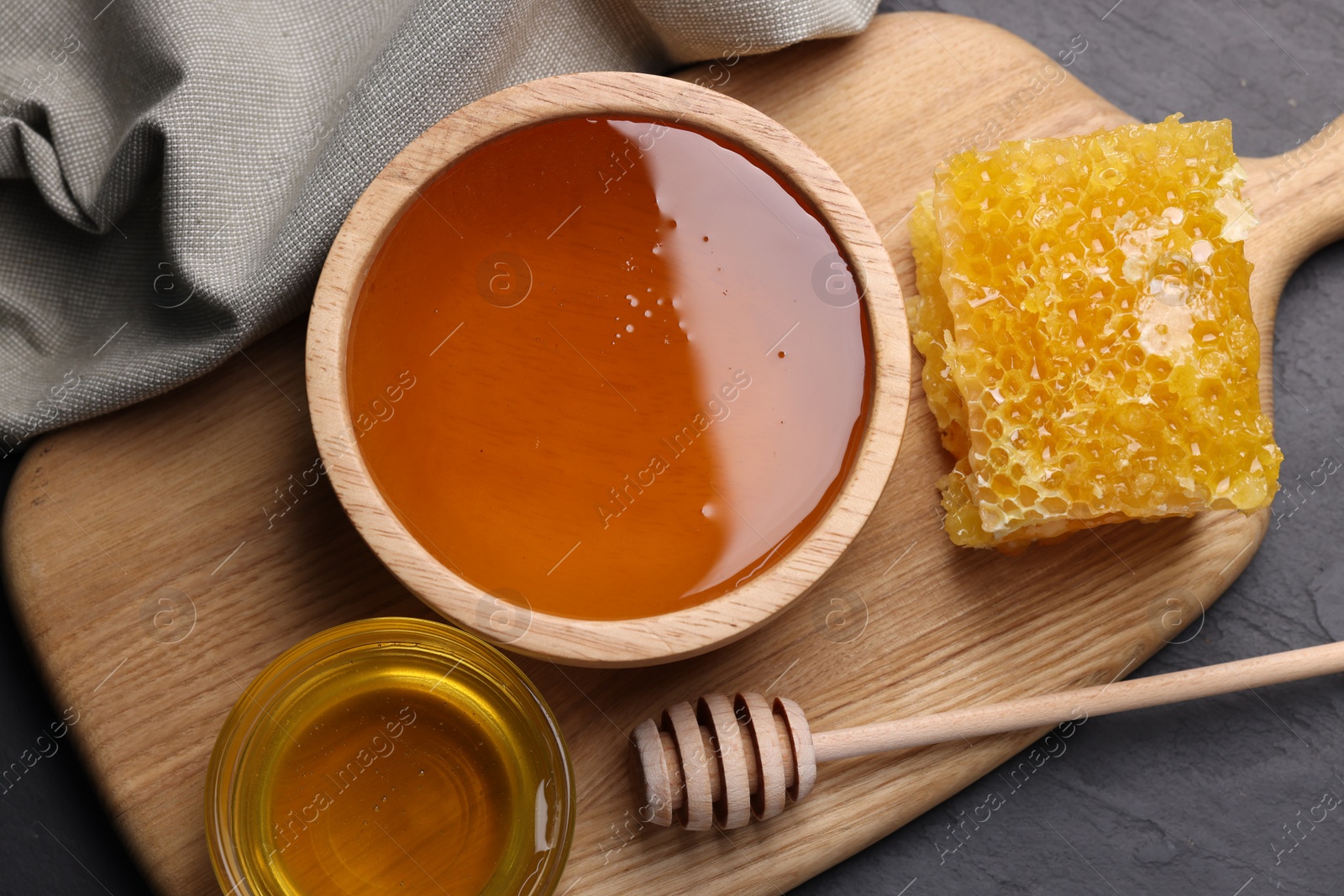 Photo of Sweet honey in bowls, dipper and pieces of honeycomb on grey table, flat lay