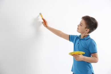 Photo of Little child painting on white wall indoors. Space for text