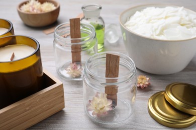 Photo of Glass jars with wicks and flowers on light wooden table. Making homemade candles