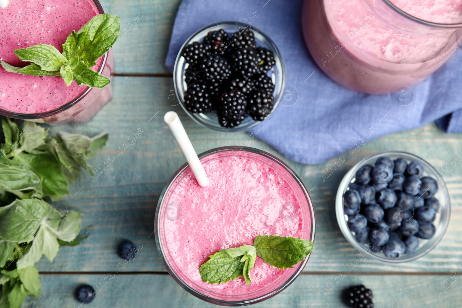 Photo of Tasty fresh milk shakes with berries on light blue wooden table, flat lay