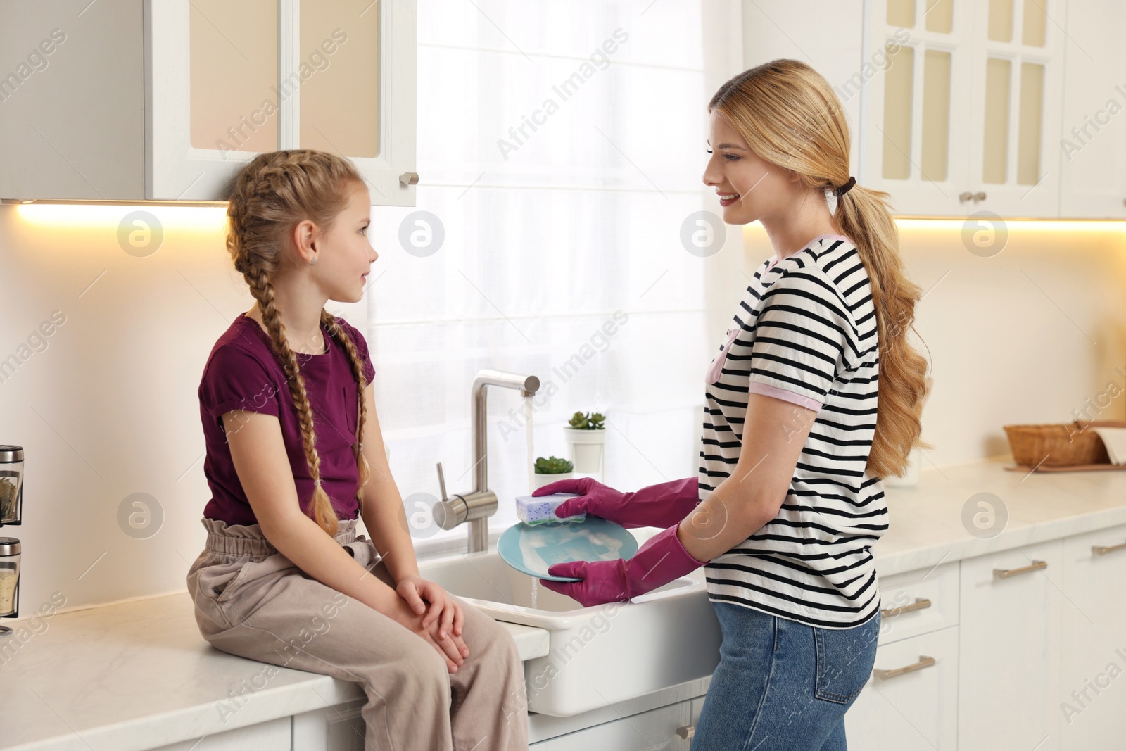 Photo of Mother washing plate while speaking with daughter in kitchen