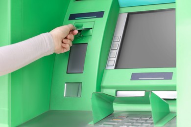 Photo of Woman inserting credit card into green cash machine, closeup