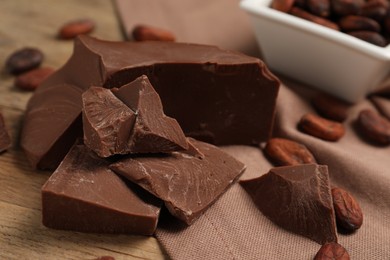 Photo of Pieces of tasty milk chocolate and cocoa beans on table, closeup