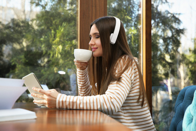 Photo of Woman listening to audiobook at table in cafe