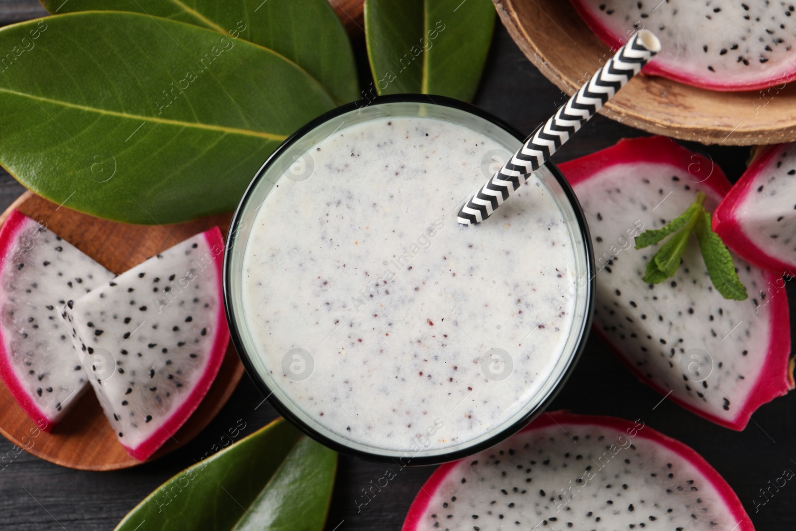 Photo of Delicious pitahaya smoothie and fresh fruits on black wooden table, flat lay