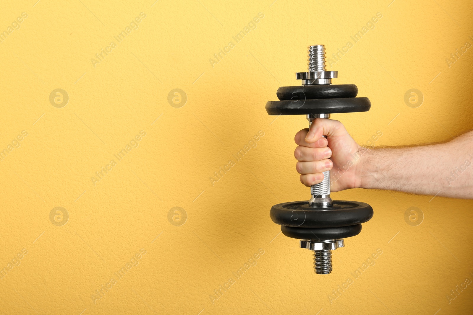 Photo of Male athlete holding metal dumbbell on color background. Space for text