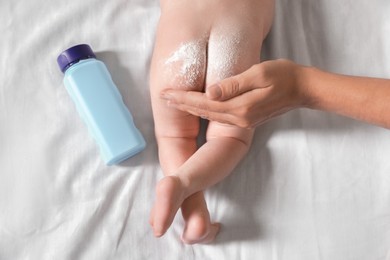 Photo of Mother applying dusting powder onto baby`s buttocks on bed, top view