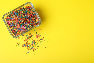 Photo of Colorful sprinkles in bowl on yellow background, top view with space for text. Confectionery decor