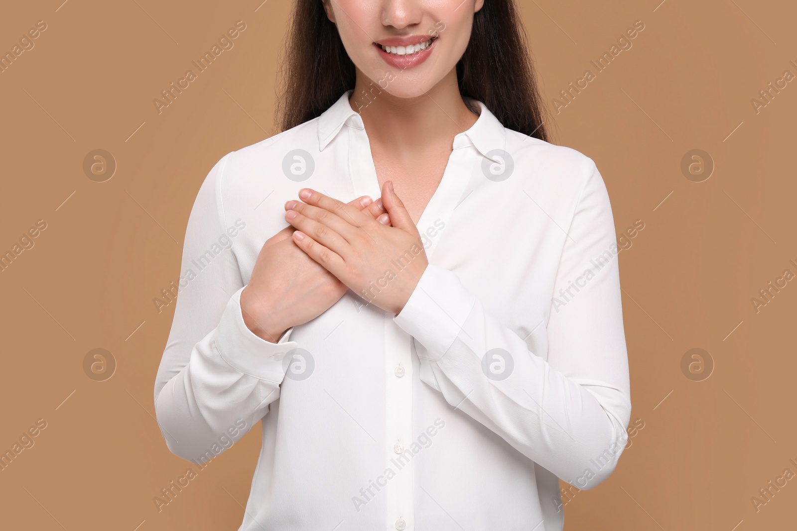 Photo of Thank you gesture. Grateful woman with hands on chest against brown background, closeup