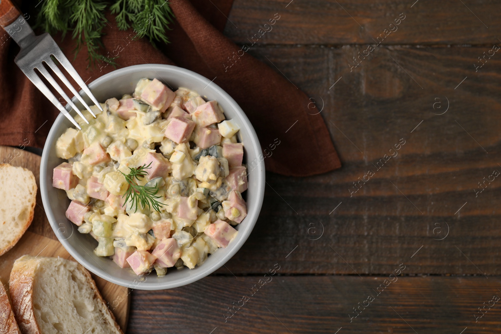 Photo of Tasty Olivier salad with boiled sausage in bowl served on wooden table, flat lay. Space for text