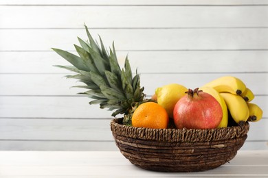 Photo of Wicker bowl with different ripe fruits on white wooden table. Space for text