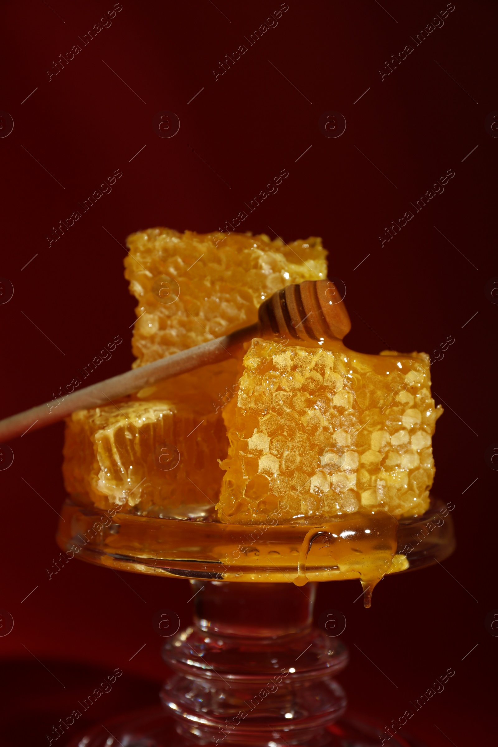 Photo of Natural honeycombs and wooden dipper on glass stand against burgundy background