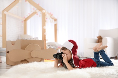 Cute little boy playing with binoculars and cardboard airplane in bedroom