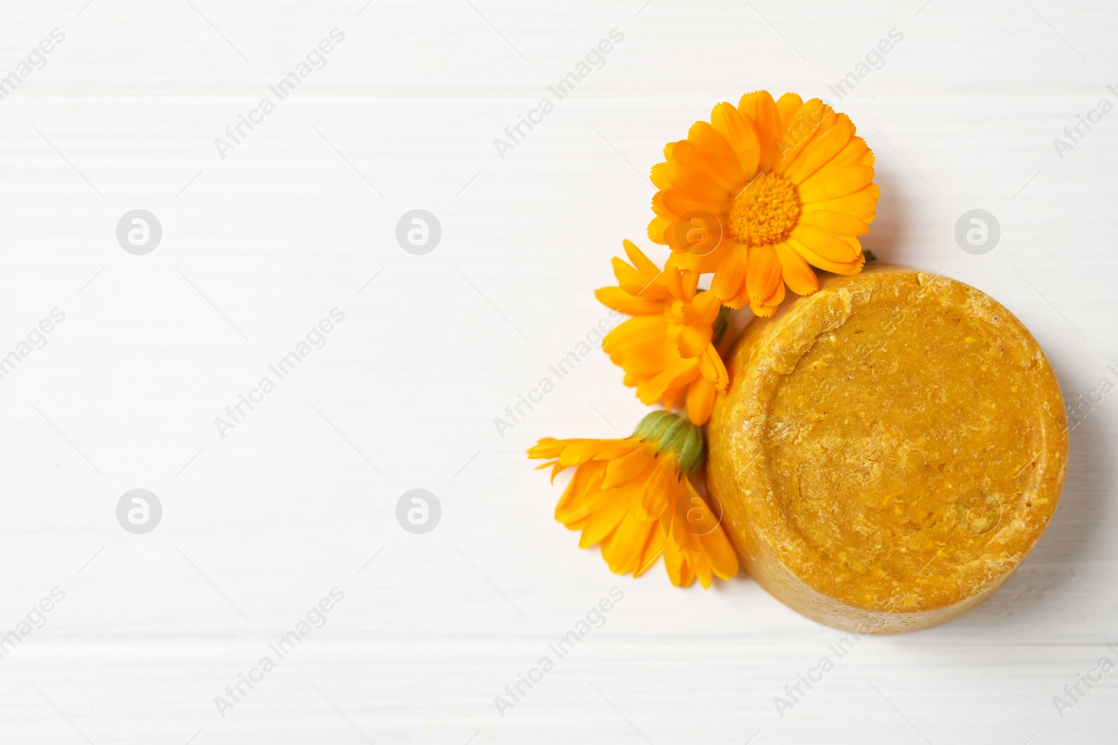 Photo of Yellow solid shampoo bar and flowers on white wooden table, flat lay. Space for text