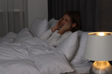 Little girl suffering from headache in bed at night