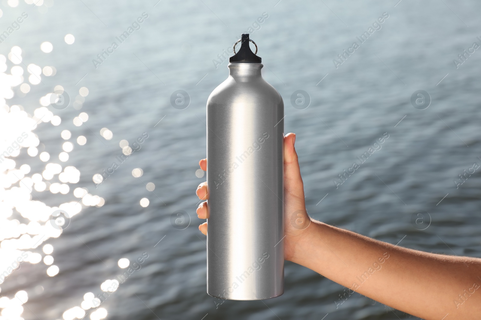 Photo of Young sporty woman holding water bottle near river on sunny day