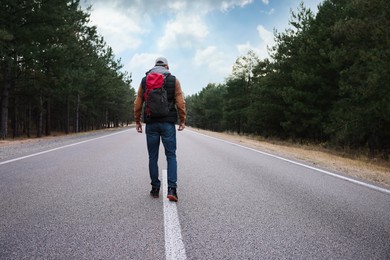 Photo of Man with backpack going along road near forest, back view