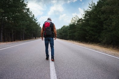 Man with backpack going along road near forest, back view