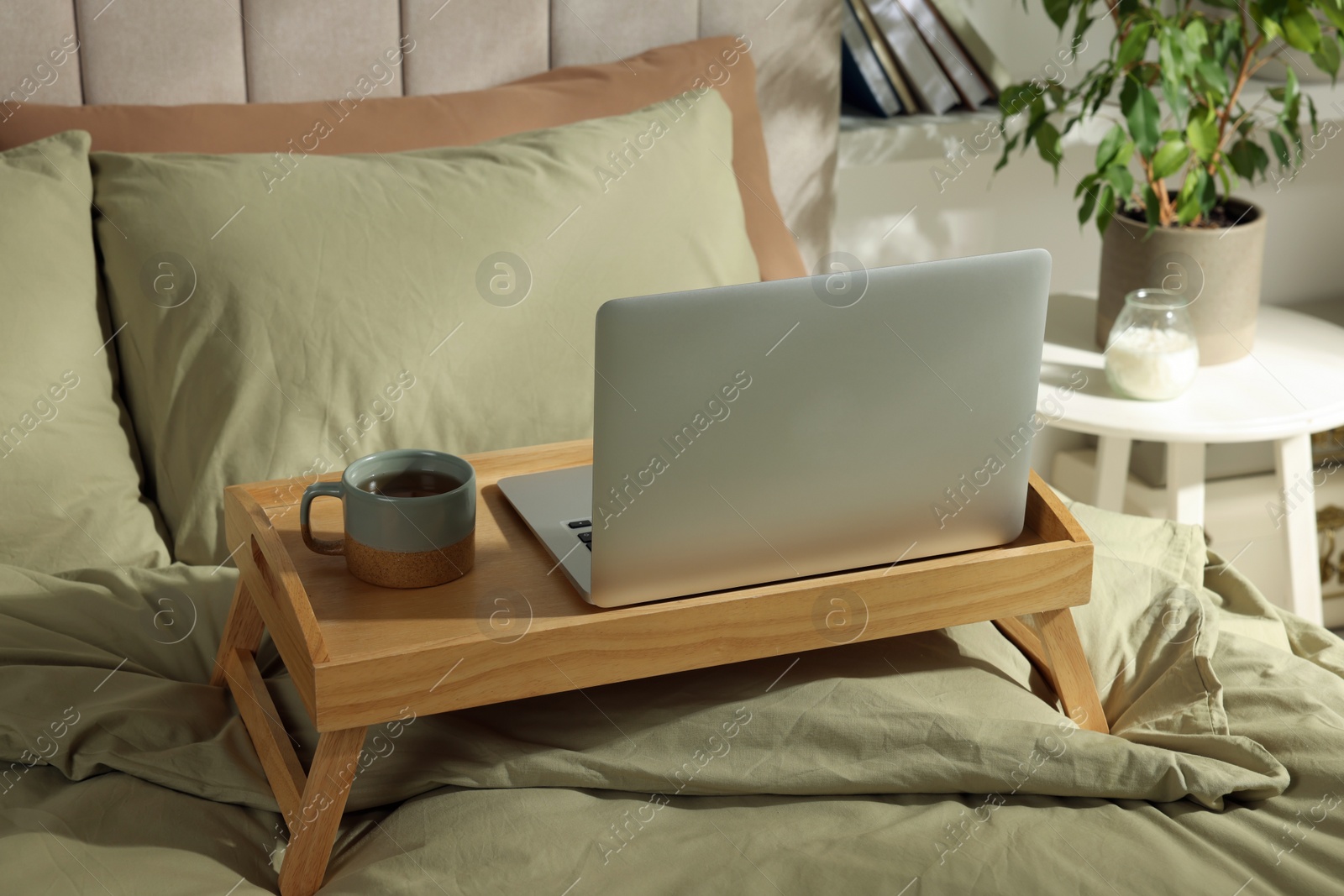 Photo of Wooden tray with modern laptop and cup of aromatic tea on bed indoors