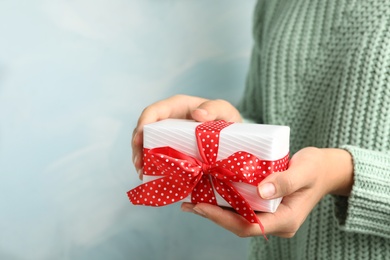 Photo of Woman holding beautiful Christmas gift on light blue background, closeup