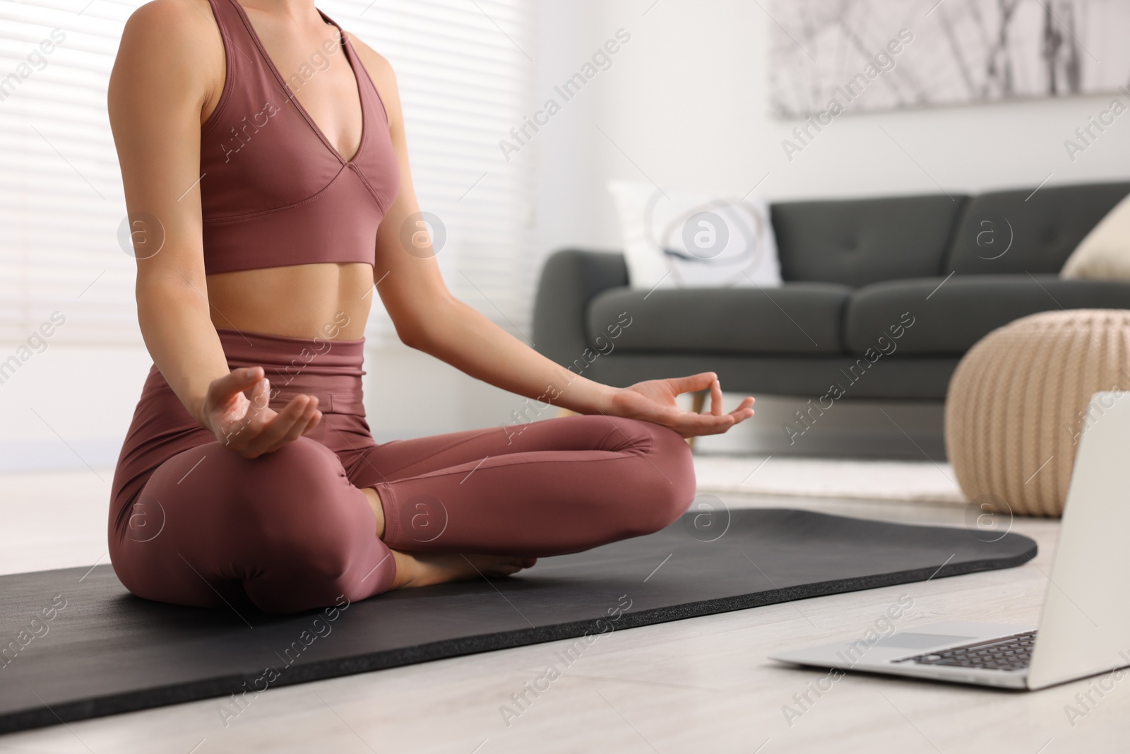 Photo of Woman practicing Padmasana with laptop on yoga mat at home, closeup. Lotus pose